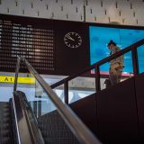 编辑部成员在双屏设备前比对信息，右侧屏幕显示公开页面截图，左侧是核对用的笔记文档，桌面整洁光线柔和的场景